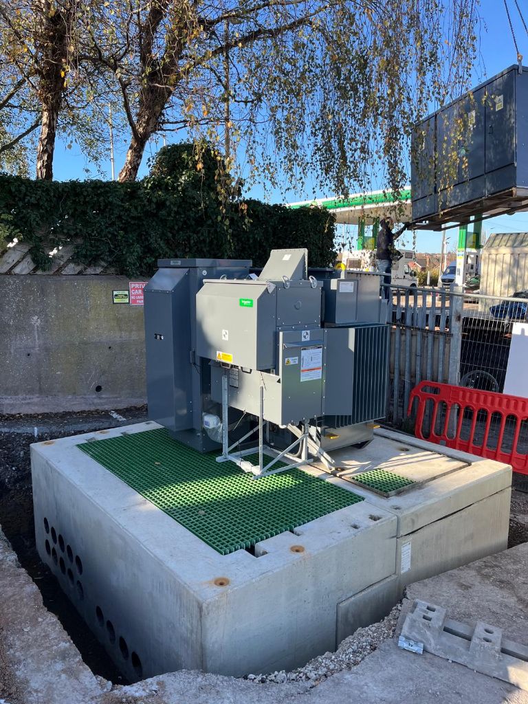Transformer unit fully installed on its concrete plinth with the BP petrol station canopy visible behind — Coseley hub under construction
